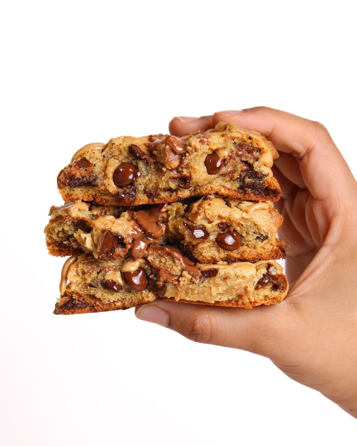 A hand holding three Berloom chocolate chip cookies, broken open and stacked